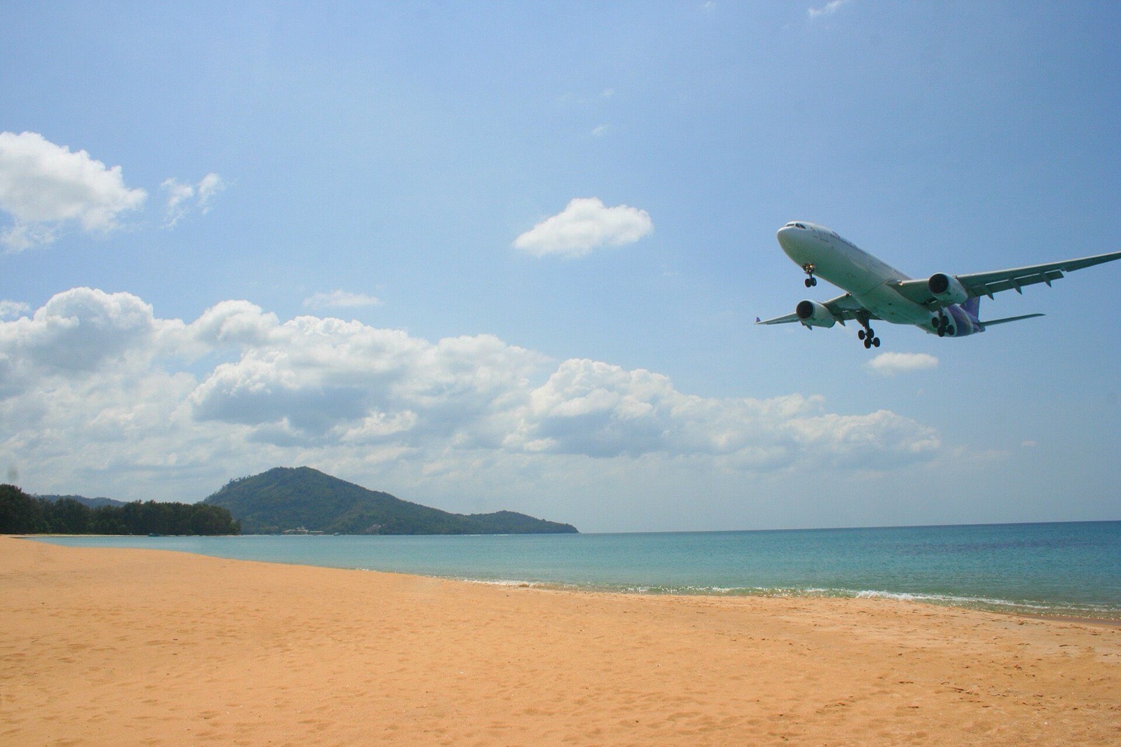 เครื่องบินการบินไทยกำลังร่อนลงจอดเหนือหาดไม้ขาว ข้างทางวิ่งของท่าอากาศยานภูเก็ต